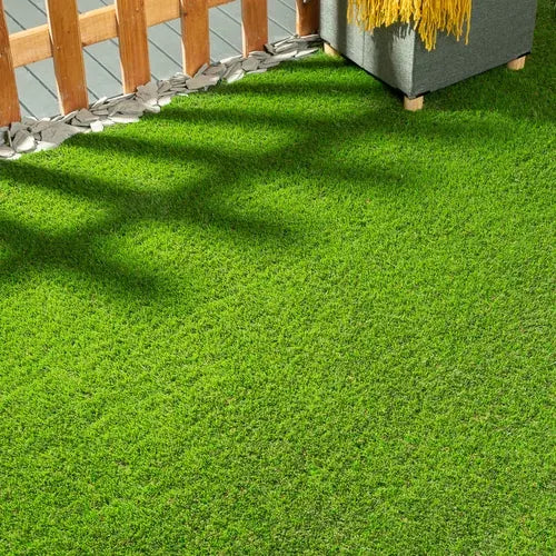 Artificial grass lawn in dappled shade beside a wooden fence and white pebbles